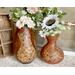 This shows a pair of gourd vases. Each vase is a warm brown and has decorative cats drawn on them. Each vase has a faux flower arrangement. 